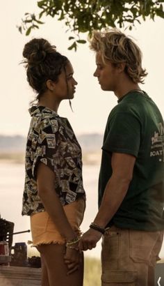 a man and woman standing next to each other in front of a body of water