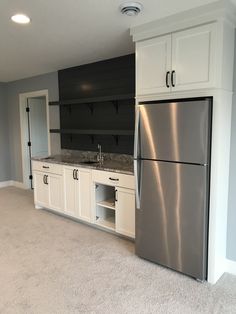 an empty kitchen with stainless steel refrigerator and white cabinets in the middle of carpeted flooring