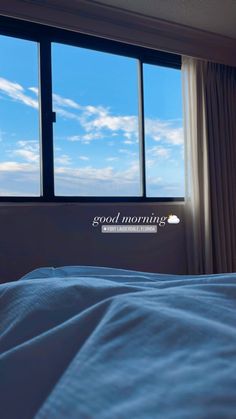 a bed sitting in front of a window under a blue sky with clouds and the words good morning on it