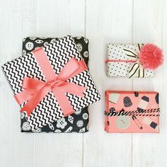 two wrapped presents are sitting next to each other on a white wooden surface with pink pom poms