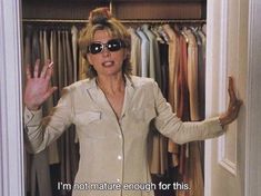 a woman wearing sunglasses standing in front of a closet full of clothes and holding her hands out