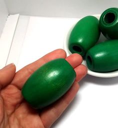 a hand is holding some green beads in a bowl