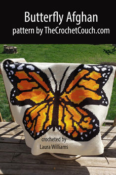 A vibrant, single crochet afghan featuring a detailed monarch butterfly design drapes gracefully over an outdoor deck railing. The bright orange and black butterfly contrasts beautifully against the natural wood Crochet Butterfly Pillow, Crochet Butterfly Blanket, April Butterfly, Butterfly Afghan, Yarn Bobbins, Tunisian Simple Stitch, Butterfly Blanket, Crochet Pattern Written, Butterfly Monarch