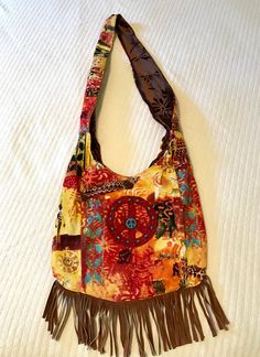 "Super cool. 100% up-cycled, cross-body shoulder bag! Exterior of this bag is multi colored corduroy, colors of red, brown, orange, yellow, gold, and turquoise. Brown sued fringe across the bottom, red felt peace sign with wooden  turquoise and copper beads. 2 tiny pockets on the back of the bag. Closes with a cocnut shell bead and brown satin ribbon. The interior is brown embossed velvet, with a beautiful daisy design! Stitched into the strap are the words \"Love and compassion are necessities, Hippie Multicolor Shoulder Bag With Adjustable Strap, Bohemian Multicolor Hobo Bag With Adjustable Strap, Red Bohemian Shoulder Bag With Tassels, Multicolor Hippie Hobo Bag, Hippie Brown Crossbody Shoulder Bag, Yellow Bohemian Festival Bags, Multicolor Fringe Bags For Festival, Colorful Bohemian Shoulder Bag With Adjustable Strap, Brown Hippie Shoulder Bag With Adjustable Strap