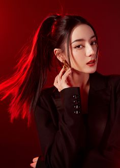 a woman with long black hair and gold hoop earrings on her left ear is posing in front of a red background