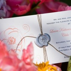 a close up of a wedding card with a wax seal on it and flowers in the background