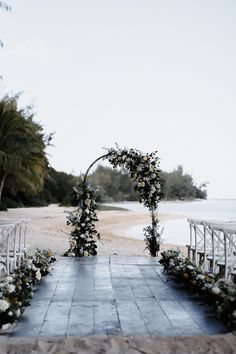 an outdoor ceremony set up with white flowers and greenery on the aisle leading to the beach