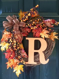 a wreath that has the letter r on it and is decorated with fall leaves, berries, and acorns