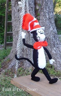 a crocheted cat in the hat on a swing next to a tree trunk