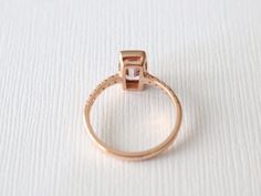 14K rose gold bezel ring featuring a natural emerald cut champagne pink sapphire measuring 8.5 x 4.2 mm and weighing 1.08 ct. (VS). This beautiful gem is further adorned and complimented by round brilliant cut diamonds with a total weight of 0.15 ct.. (G,VS2/SI1) 2.0 mm comfort fit band, size 6, can be sized up to 8. Original Studio 1040 design. *Ready to ship SKU 5-100117 Emerald Cut Rose Gold Jewelry With Halo Design, Rose Gold Emerald-cut Jewelry With Halo Setting, Emerald Cut Rose Gold Halo Jewelry, Rose Gold Baguette Cut Ring With Rose Cut Diamonds, Minimalist Emerald Cut Rose Gold Ring, Rose Gold Asscher Cut Gemstone Ring, Minimalist Rose Gold Emerald Cut Ring, Emerald Cut Rose Gold Diamond Ring With Halo Setting, Radiant Cut Rose Gold Ring With Gemstone