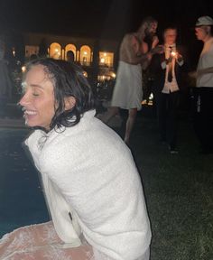 a woman sitting on the ground next to a pool at night with other people around her