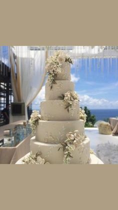 a white wedding cake with flowers on it sitting in front of an ocean view window