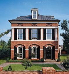 a large brick house with black shutters on the front and side windows, surrounded by greenery