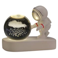 an astronaut holding the hand of a snow globe with rain coming from it, on a white base