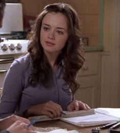 a woman sitting at a kitchen table with a notebook and pen