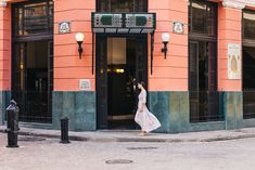 a woman walking down the street in front of an orange and green building with black doors