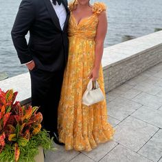 a man and woman standing next to each other on a pier near the water wearing formal attire