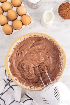 a bowl filled with chocolate frosting next to eggs