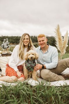 a man and woman sitting on a blanket with a dog