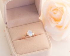 an open ring box with a white rose in it and a pink flower on the side