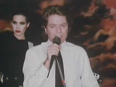 a man holding a microphone while standing next to a woman with makeup on her face