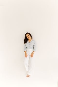 a woman standing in front of a white wall with her hands on her hips and smiling