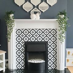 a fireplace with black and white tiles on the mantle, potted plants and mirror above it