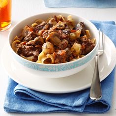 a white bowl filled with pasta and meat on top of a blue napkin next to a fork