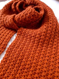 an orange crocheted scarf laying on top of a bed