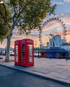 a red phone booth sitting on the side of a road next to a ferris wheel