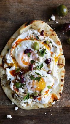 an egg and olive pizza is shown on a wooden table next to some olives