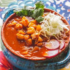 a blue bowl filled with food on top of a colorful table cloth next to a spoon