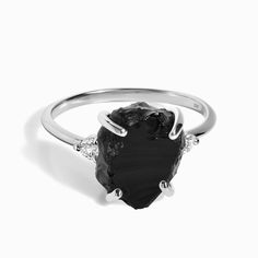 a black stone ring sitting on top of a white surface with two diamonds around it