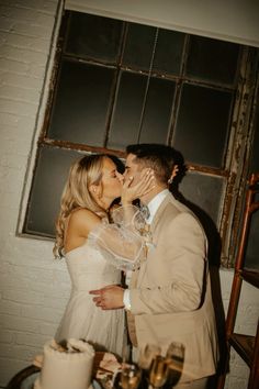 a bride and groom kissing in front of a window at their wedding reception with cake