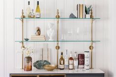 a shelf filled with bottles and glasses on top of a white counter next to a vase