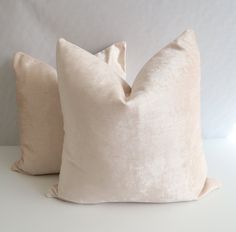 two pillows sitting on top of a white table next to each other, one has a light colored pillow