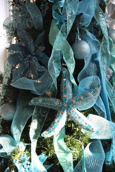 a christmas tree decorated with blue and green ribbons, starfish ornament and ornaments