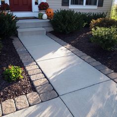 a walkway leading up to a house with pumpkins on the front door and bushes