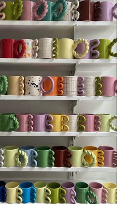 many different colored coffee mugs are on the shelves in front of eachother