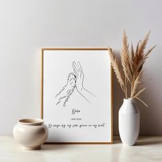 a white vase sitting on top of a table next to a framed print with a praying hand