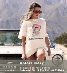 a woman sitting on the hood of a car wearing a t - shirt that says color ivory