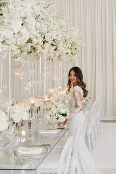 a woman standing in front of a table with white flowers and candles on top of it