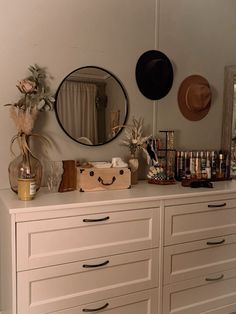 a white dresser topped with lots of bottles and drawers next to a mirror on the wall