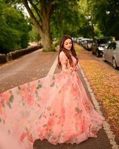 a woman in a long pink dress standing on the side of a road next to trees