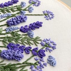 purple and green flowers are embroidered onto a white fabric with embroidery work on the hoop