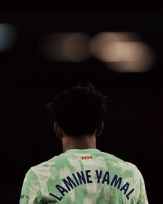 the back of a young man wearing a green and white shirt with blue writing on it