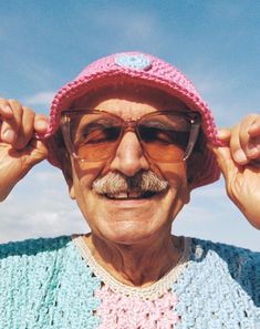 an older man with glasses and a pink hat is holding his hands up to his ears