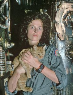 a woman holding a cat in front of an industrial machine room with pipes and wires