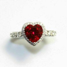 a red heart shaped diamond ring sitting on top of a white surface