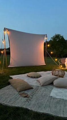 an outdoor movie screen is set up on the grass with pillows and lights around it